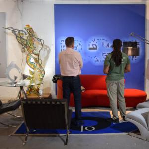 Two men viewed from behind contemplate a large blue painting and red sofa.